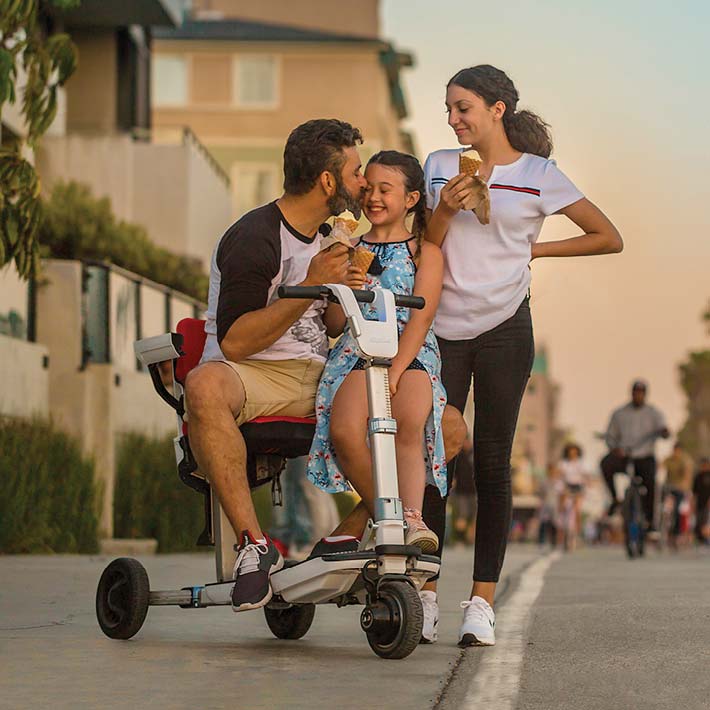 Mann auf weissem ATTO Scooter mit Familie auf der Strandpromenade, Anwendungsszene