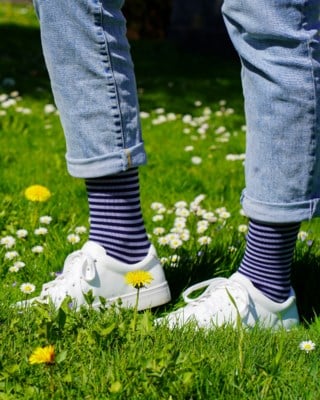 Fuesse mit blau gestreiften Stuetzstruempfen sigvaris zu Sneakers auf einer Blumenwiese
