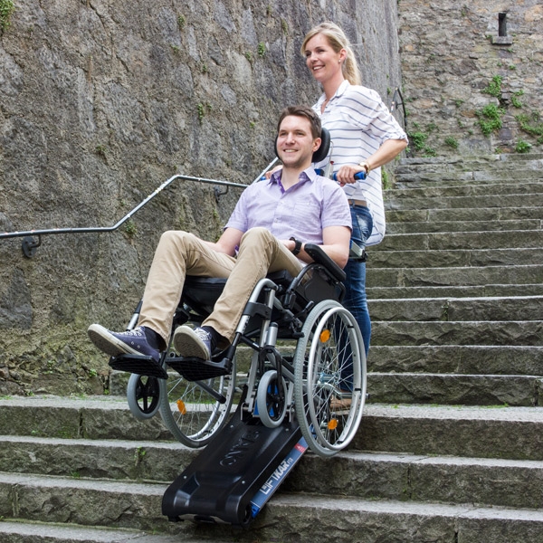 Treppenraupe Liftkar PTR 130 im Einsatz, Begleitperson fährt Rollstuhlnutzer eine Treppe hinab